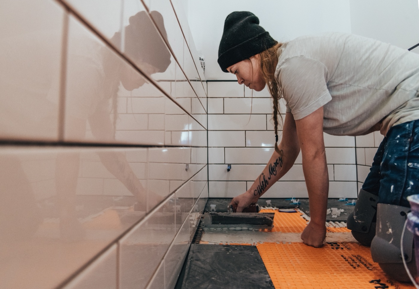 Tiler working on a white subway tile wall with dark grout lines